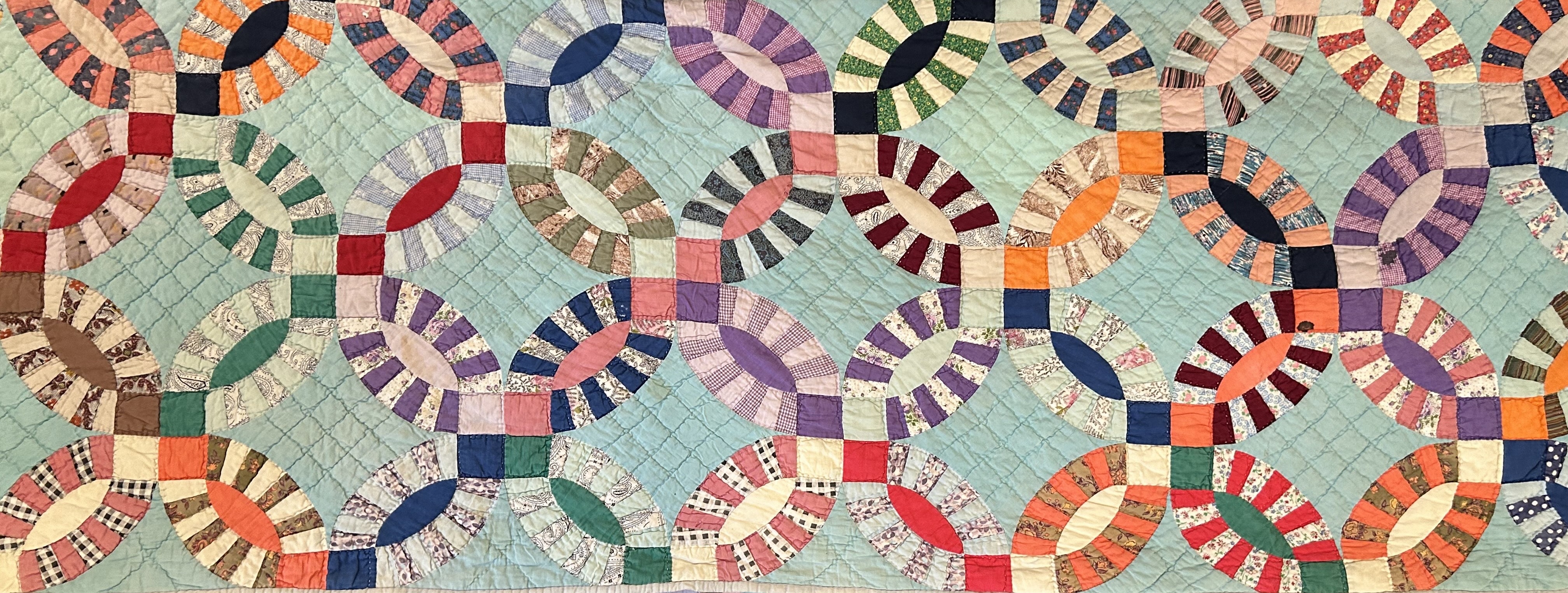 Image of a handmade double wedding band quilt featuring interlocking circular patterns in vibrant colors on a light background. The intricate stitching and carefully pieced fabric showcase the craftsmanship and artistry of traditional quilting.