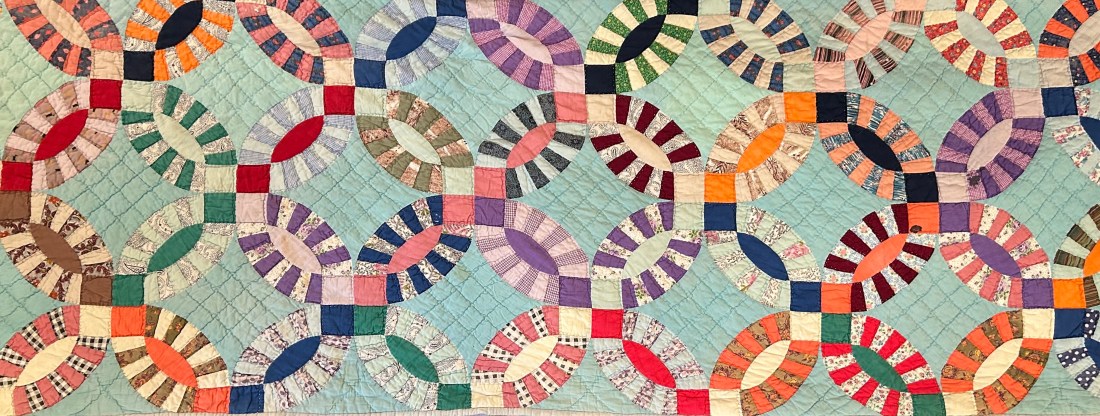 Image of a handmade double wedding band quilt featuring interlocking circular patterns in vibrant colors on a light background. The intricate stitching and carefully pieced fabric showcase the craftsmanship and artistry of traditional quilting.