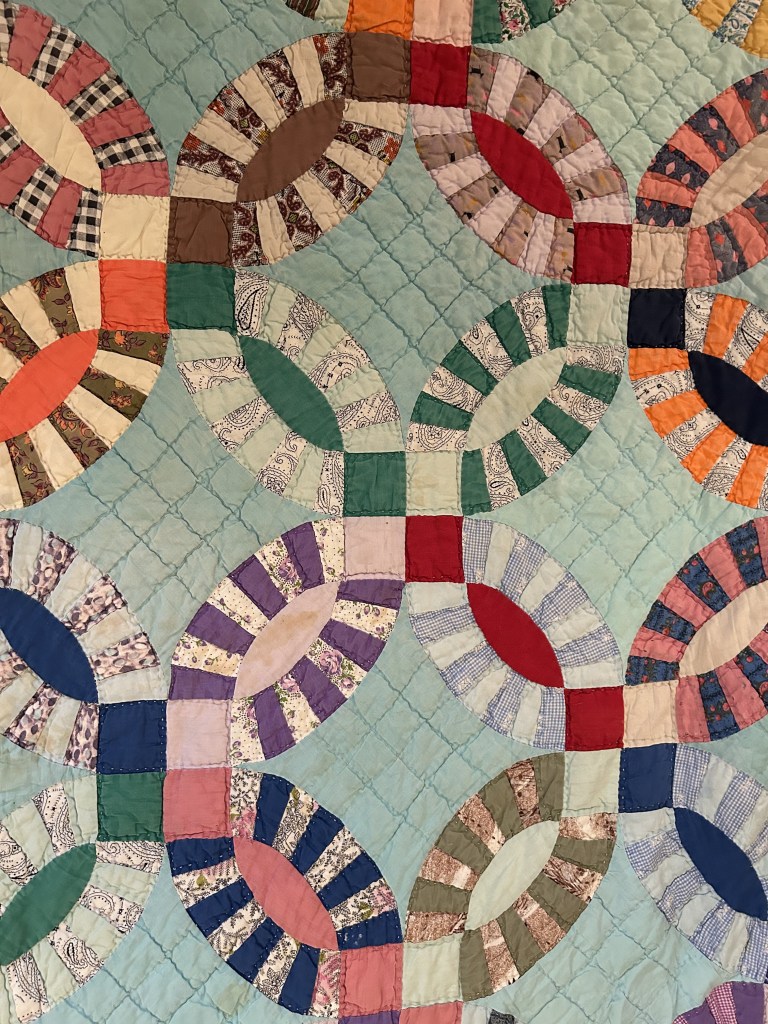 Image of a handmade double wedding band quilt featuring interlocking circular patterns in vibrant colors on a light background. The intricate stitching and carefully pieced fabric showcase the craftsmanship and artistry of traditional quilting.