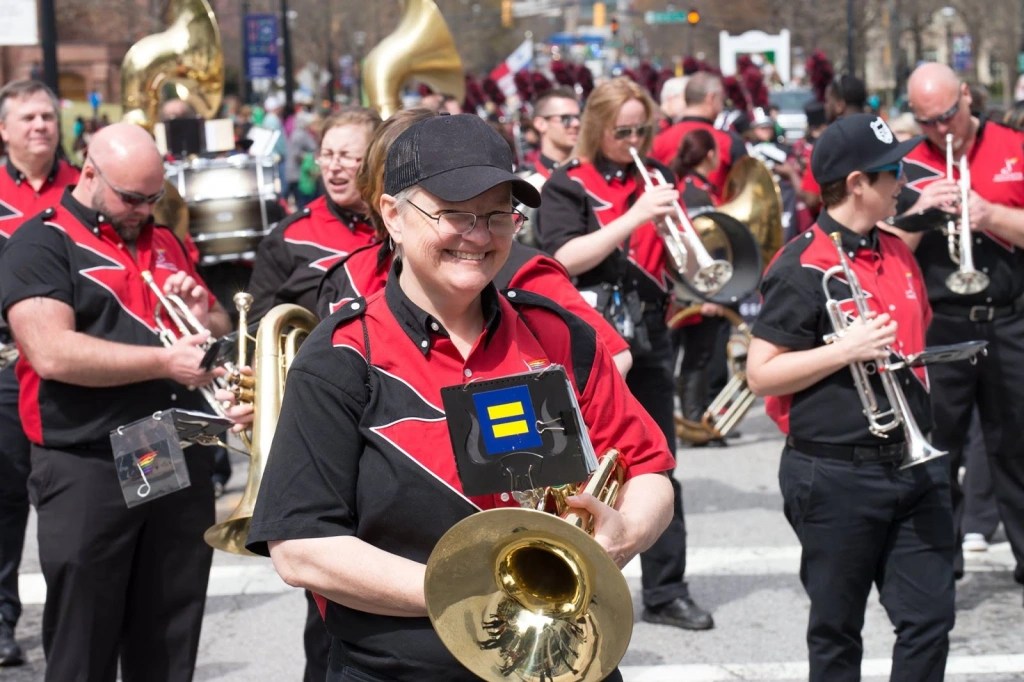Image of marching band, includes trumpet players, tuba players, and drums in background. Ugena Whitlock with mellophone in foreground.